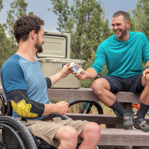 Man in wheelchair exchanging a beverage with another male